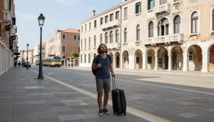 A traveller with a rolling suitcase looking relieved on a street near Venice's Santa Lucia train station, with no bridges in sight.