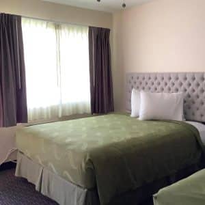 Guest room at National 9 Motel in Santa Cruz with a sage-green quilted bedspread, tufted grey headboard and large window with eggplant curtains