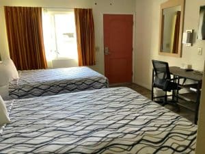 Two-Queen-Bed Room at National 9 Motel in Santa Cruz with two queen beds, sunlit orange-striped curtains, a red entry door and desk with mirror