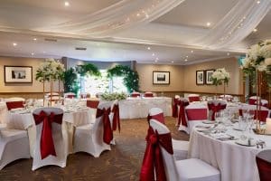 Banquet room at The Grange Manor set up with white tables and red bows for a wedding, Grangemouth