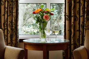 Cream and sandstone interior at The Grange Manor with a vase of flowers and two crystal glasses on a polished table, Grangemouth