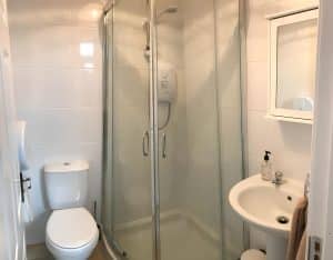 Clean shared bathroom with a corner shower, white basin and toilet, Irvine