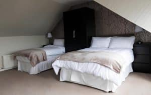 Triple room at Harbourlights with a double and single bed, soft throws and patterned feature wall under a sloped ceiling, Irvine