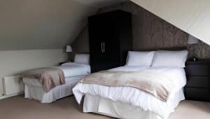 Spacious family room at Harbourlights with a double and single bed, soft throws and a feature wall, Irvine