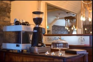 Coffee station with espresso machine and grinder beneath a stone wall and a large mirror, Irvine