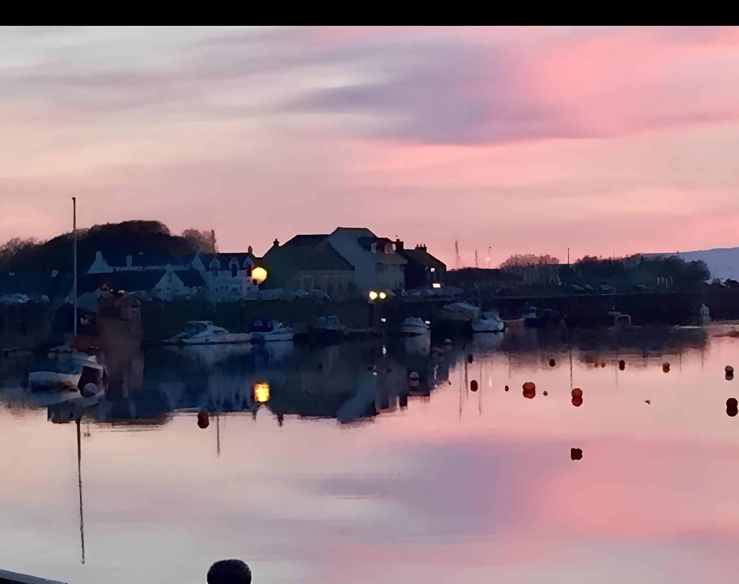 Pink dawn over Irvine harbour with the guest house lit up across calm water and moored boats, North Ayrshire