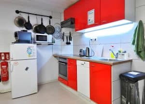 The shared self-catering kitchen with red cabinets, oven and hanging pans at Hostel Bad Goisern