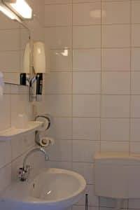 Compact white-tiled en-suite bathroom with a basin and toilet at Hotel De Koopermoolen, Amsterdam
