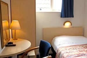 Compact single room at Hotel De Koopermoolen with a wooden bedframe, desk and lamp, Amsterdam