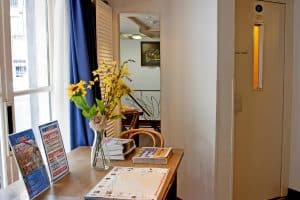 Reception corner with a fresh-flower table beside the renovated guest lift at Hotel De Koopermoolen, Amsterdam