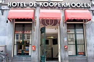 Red awnings and tall windows on the monumental Warmoesstraat facade of Hotel De Koopermoolen in central Amsterdam