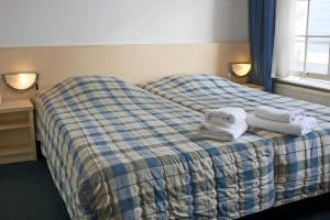 Twin beds with blue-check covers under a window in a compact room at Hotel De Koopermoolen, Amsterdam