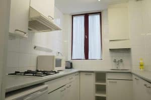 White-tiled apartment kitchenette with a hob, microwave and curtained window at Hotel De Koopermoolen, Amsterdam