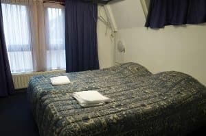 Triple room at Hotel De Koopermoolen with a patterned bedspread, towels and tall curtained window, Amsterdam
