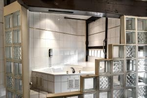 Tiled bathroom with a corner spa bath and glass-block wall in a room at Hotel De Koopermoolen, Amsterdam