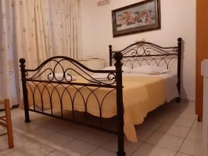 Double room at Pergola Hotel with an ornate black wrought-iron bed, yellow bedspread and a framed painting, Agios Nikolaos