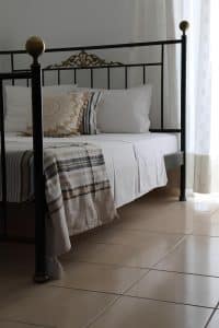 Single room at Pergola Hotel with a wrought-iron bed, white tiled floor and a framed seascape, Agios Nikolaos