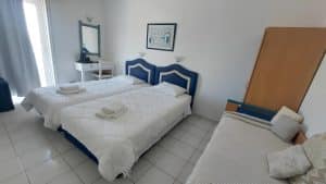 Sea-view twin room at Pergola Hotel with blue upholstered headboards, white bedding and a balcony door, Agios Nikolaos