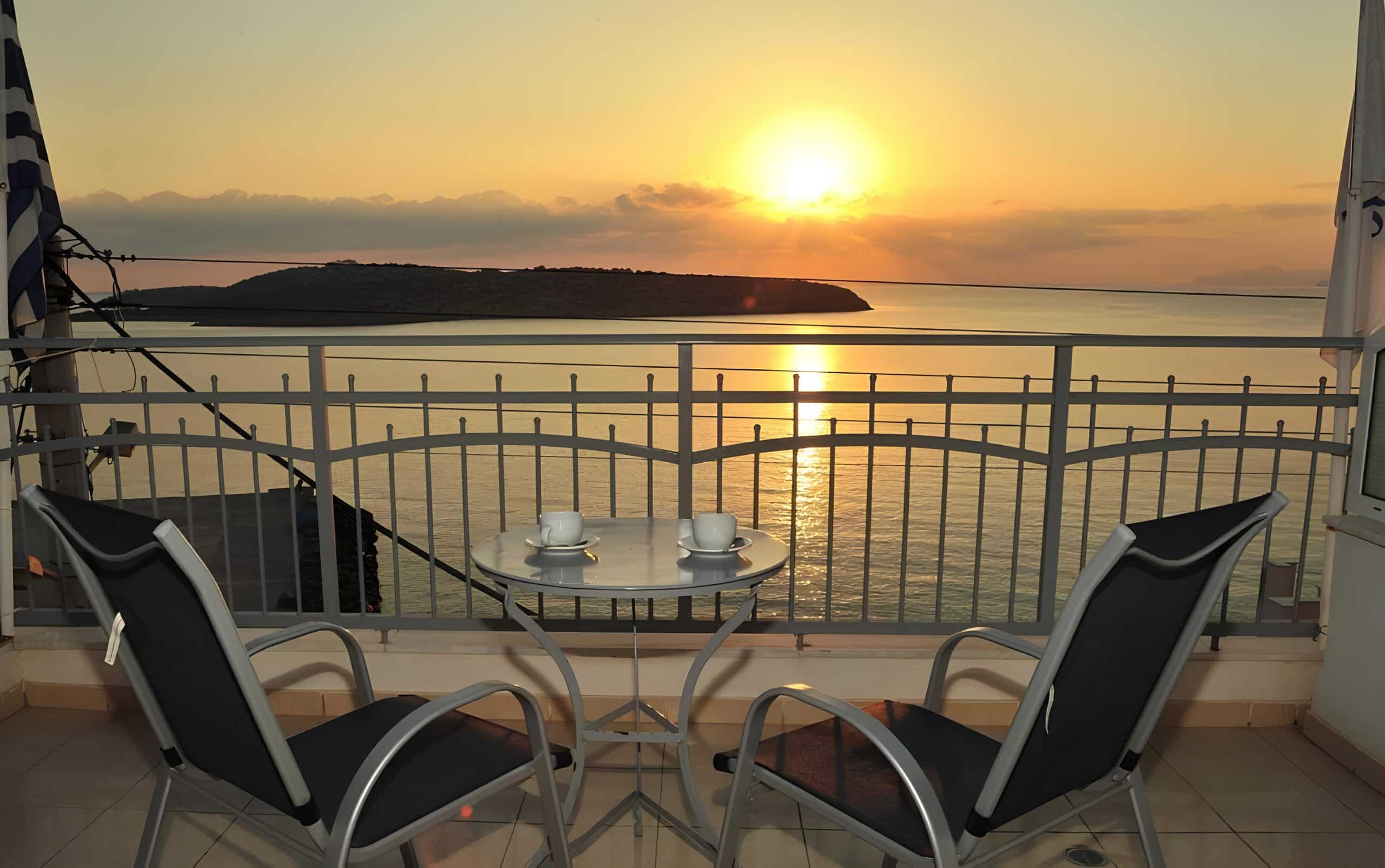 Sunrise over Mirabello Bay from a sea-view balcony at Pergola Hotel, two coffee cups on the table and the islet of Agioi Pantes beyond, Agios Nikolaos