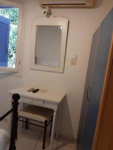 Room interior at Pergola Hotel with a white dressing table, mirror and a blue wardrobe beside a shuttered window, Agios Nikolaos
