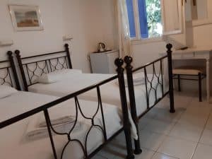 Twin room at Pergola Hotel with black wrought-iron bed frames, white tiled floor and a blue-shuttered window, Agios Nikolaos