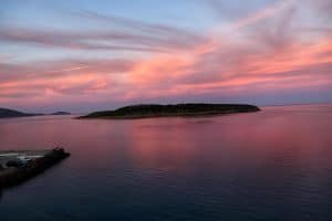Pink dawn over Mirabello Bay seen from Pergola Hotel, the islet of Agioi Pantes silhouetted on calm water, Agios Nikolaos