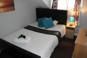 Double room at The Vale Apart Hotel with a leather headboard, teal cushions and a floral curtain, Hull