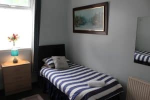Single room at The Vale Apart Hotel with a blue-striped bed, a framed cityscape print and a bright window, Hull