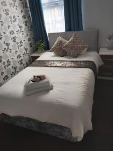 En-suite double room at The Vale Apart Hotel with a grey upholstered headboard, damask feature wall and teal curtains, Hull