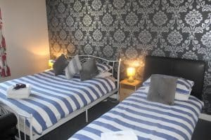 Triple room at The Vale Apart Hotel with a white metal day bed and a single bed against a silver damask wall, Hull