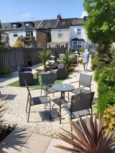 Sunny gravel garden with rattan seating, palms and patio tables behind The Vale Apart Hotel, Hull