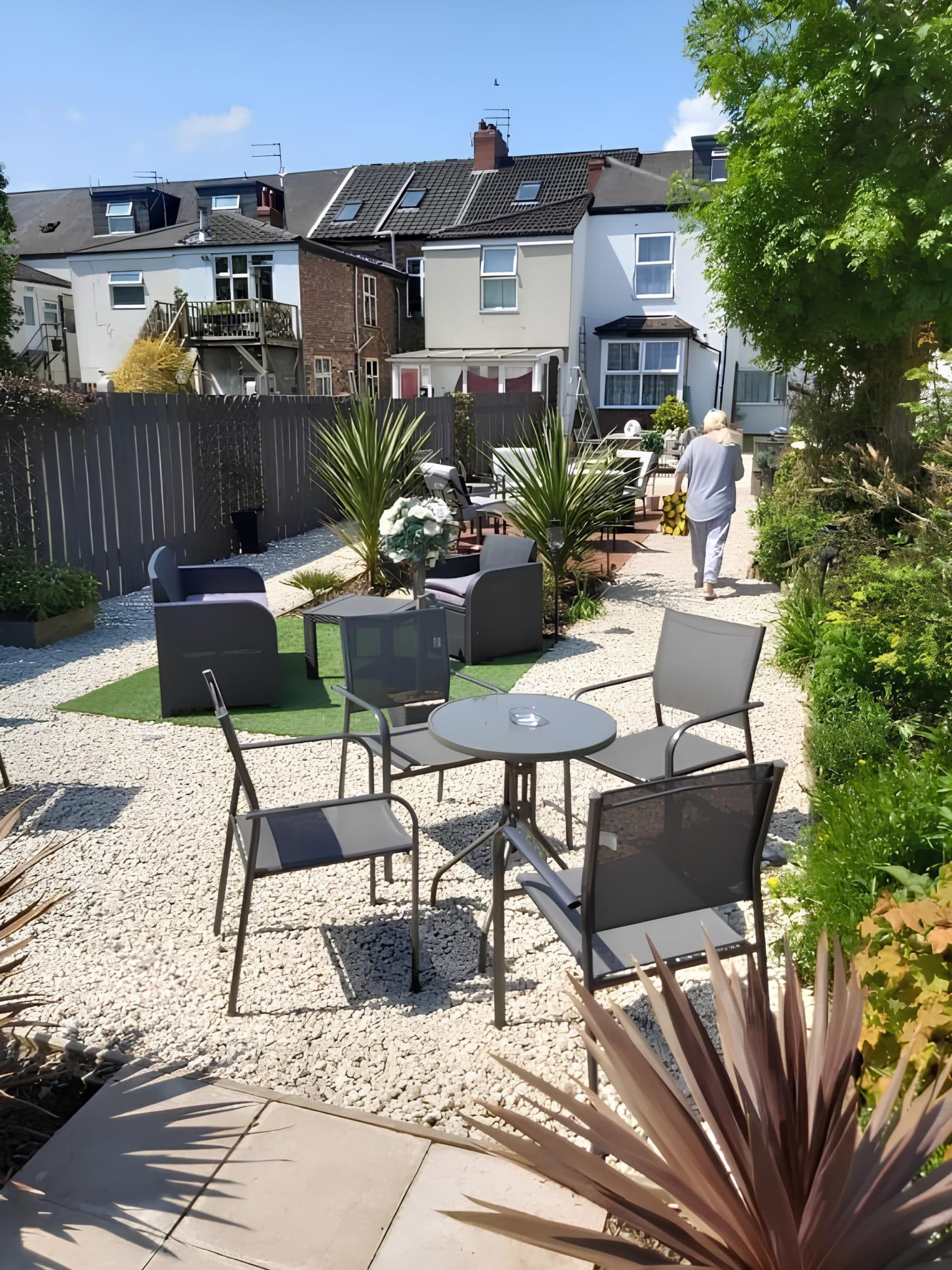 Sunny gravel garden with rattan seating, palms and patio tables behind The Vale Apart Hotel, Hull
