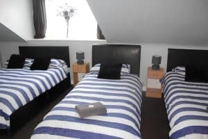 En-suite triple room at The Vale Apart Hotel with three blue-striped single beds and a flowered window, Hull