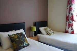 Twin room with grey leather headboards, a green lamp and floral curtains at The Vale Apart Hotel, Hull