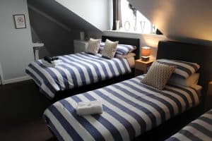 En-suite twin room at The Vale Apart Hotel with two blue-striped beds, gold cushions and a LOVE sign on the sill, Hull