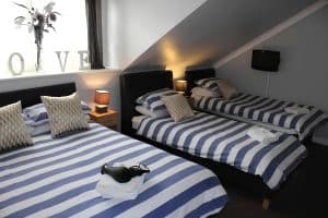 Family room at The Vale Apart Hotel with a double and two single beds in blue stripes under a sloped ceiling, Hull