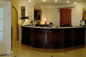 A traditional hotel reception desk in dark wood with a marble top, staffed by one receptionist
