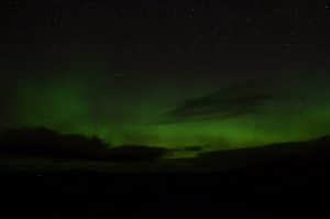 Green aurora low across the northern horizon under stars in Sutherland, the northern lights from an Inverness base