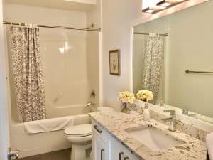 A guest bathroom with a bath and shower behind a floral curtain, a granite vanity and fresh flowers