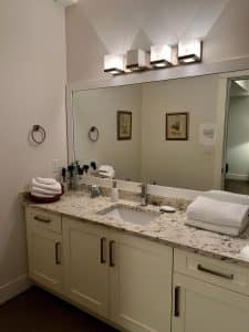A long granite vanity under a five-bulb light bar, with folded towels and toiletries