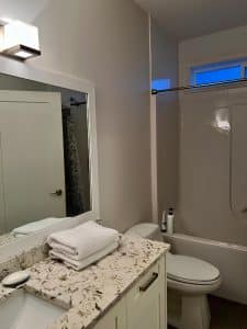 A guest bathroom with a bath and shower, granite vanity and folded white towels
