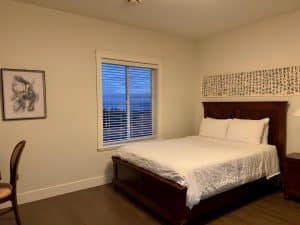 A guest room at Ocean Melody Vacation Rooms with a dark wood sleigh bed, white bedding and a window looking out to the sea