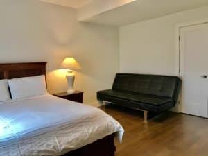 The second guest room at Ocean Melody Vacation Rooms with a double bed, a bedside lamp and a black leather sofa bed