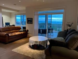 The shared lounge at Ocean Melody Vacation Rooms with leather sofas, a round glass table and sliding doors opening to the sea-view balcony