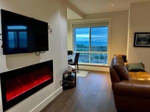 A wall-mounted television and electric fireplace in the shared lounge, with windows looking west to the sea