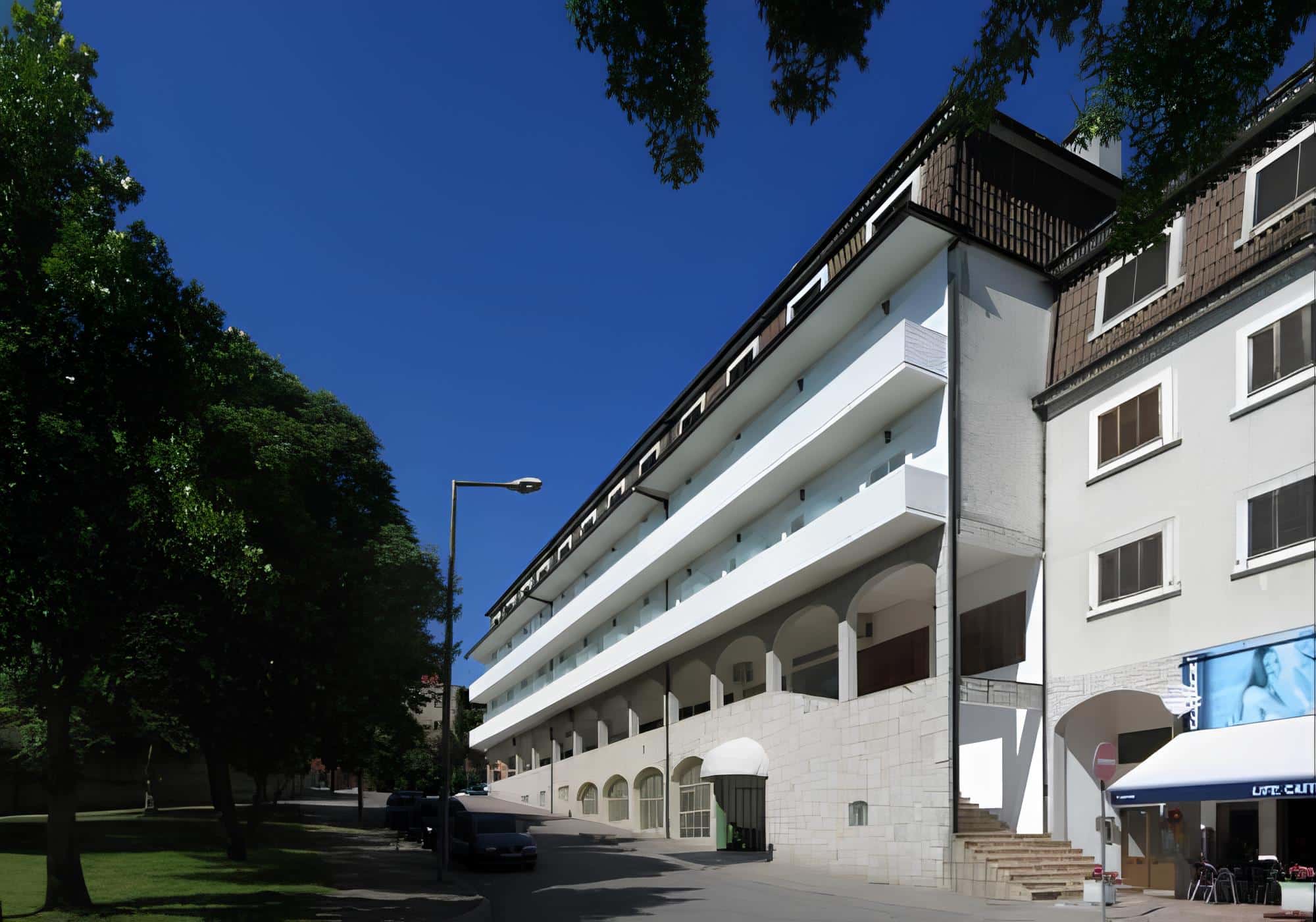 The white facade and stone arcade of the Petrus Hotel in Chaves, seen from the tree-lined street on a bright day