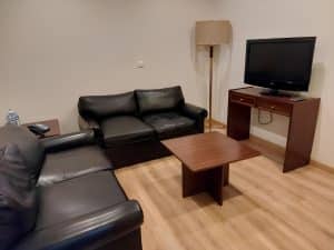 A sitting area at the Petrus Hotel with black leather sofas, a coffee table and a television on a desk