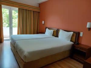 A room at the Petrus Hotel with two beds pushed together against an orange feature wall and doors opening onto a balcony