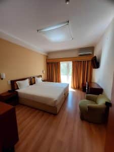 A suite at the Petrus Hotel with a double bed, a green armchair and full-height curtains at the balcony doors