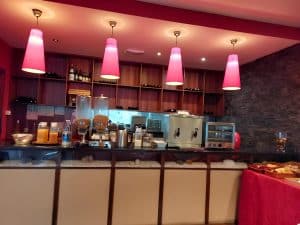 The serving counter at the Petrus Hotel under pink pendant lights, with juice and coffee machines